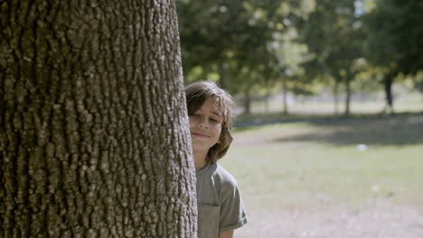 Medium-shot-of-cheerful-boy-peeping-out-of-tree-and-smiling